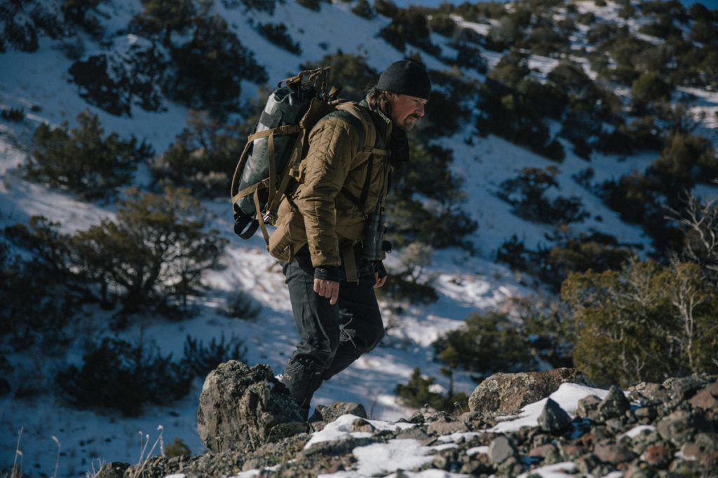 Casey Anderson with a backpack scrambling up snowy rocks